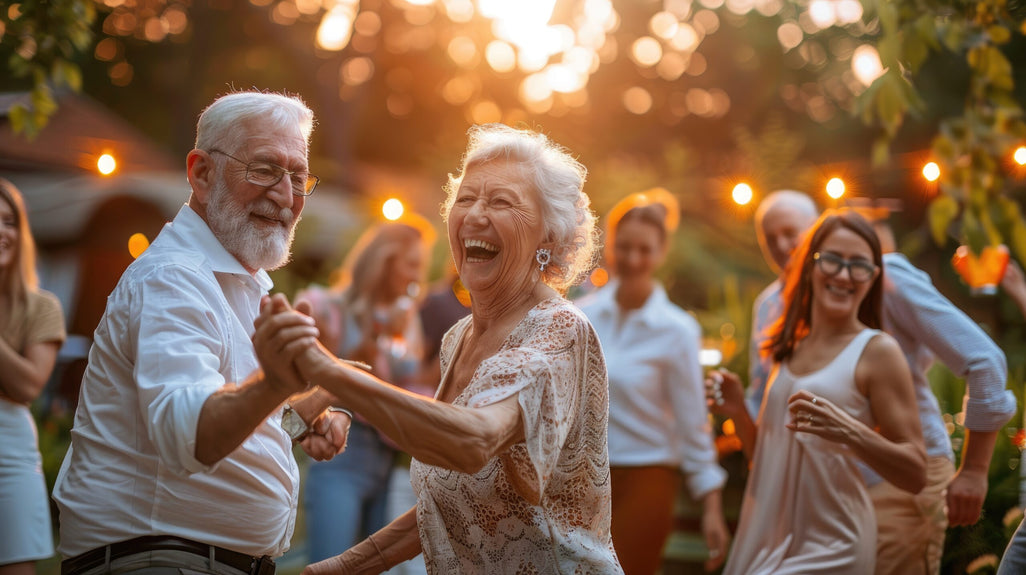 An elderly couple dances happily outdoors at sunset, surrounded by smiling people in a garden. Warm lights create a festive atmosphere.