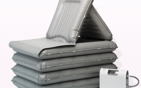 A stack of grey inflatable air mattresses with one folded as a chair. Nearby is a white pump with a hose for inflation.