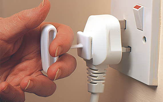 A person using a special tool to safely unplug a white three-pin plug from a wall socket, avoiding direct contact with the plug.