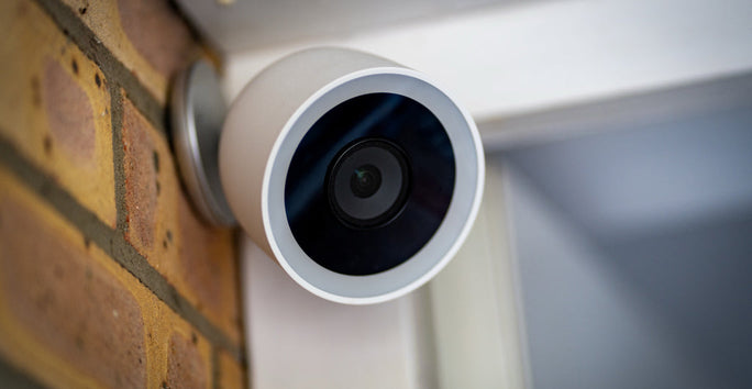 A round white security camera with a dark lens is mounted on a brick wall, angled downward to monitor the area.