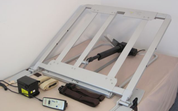 An adjustable electric bed mechanism is displayed, featuring metal rails and a control unit. A handheld remote with buttons and wires is connected to the setup, which rests on a beige mattress.