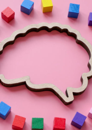 A wooden brain shape is surrounded by colorful cubes on a pink background, creating a playful and educational scene. Image