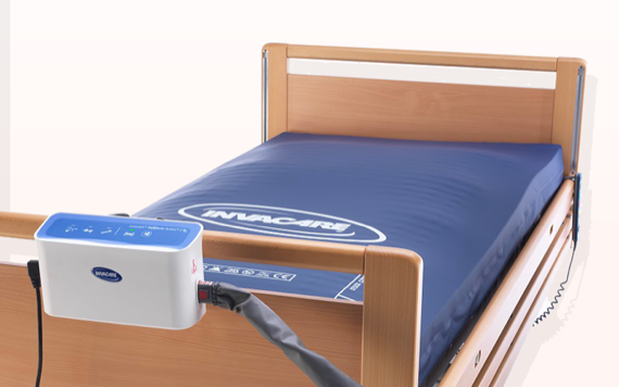 A wooden hospital bed with a blue air mattress and a control unit connected by a gray hose, showing buttons and indicators.