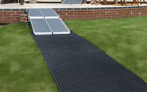A foldable metal ramp leads down to a textured black mat on a grassy lawn, extending from a brick patio.