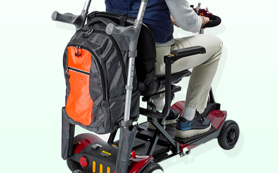 A person on a black and red motorized scooter with a backpack; wearing beige pants and dark shoes.