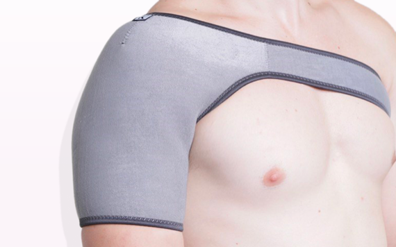 A person wearing a grey shoulder support brace on their left shoulder, covering the upper arm and chest, against a light background.