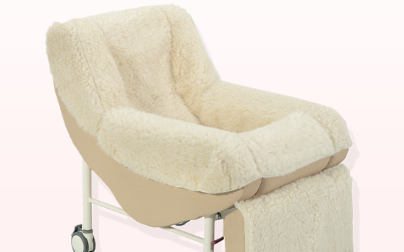 A plush, beige chair with fluffy upholstery and a white metal frame with wheels, against a light pink background.