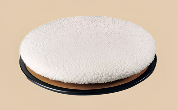 A round, fluffy, white cushion on a black base against a beige background. It appears soft and resembles plush fabric.