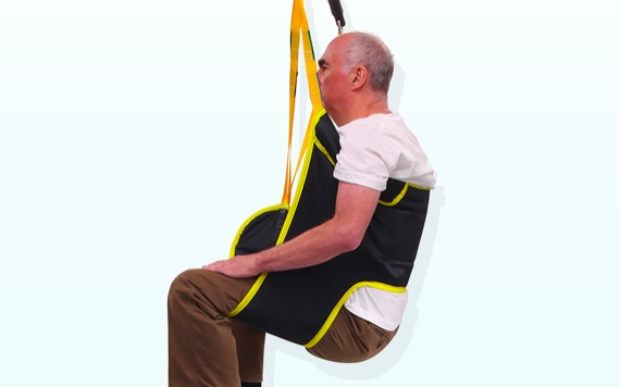An older man sits in a lift sling with colorful straps, looking relaxed and safe, demonstrating a mobility aid against a light background.