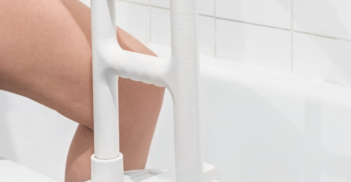 A person stepping into a white bathtub using a grab bar. White walls with tiles are visible in the background.