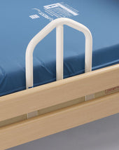 Grab handle fitted to Bradshaw bed with blue mattress and light wood frame, shown for transfer support, side view.