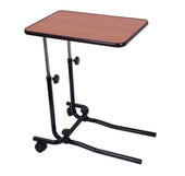 Adjustable overbed table with brown top, black frame and wheels, shown at base of a divan bed, angled side view.