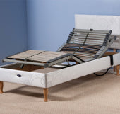 Restwell Devon electric adjustable bed base with wooden legs and slatted frame in a carpeted room with blue walls, front view.