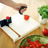Etac Food Preparation Board in use, tomato being sliced with chopped tomatoes and basil plant nearby, close-up view.