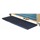 Navy blue tri-fold crash mattress with foam padding placed by a hospital bed, fall protection pad, side view.