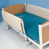 Hospital bed with high Sidhil Universal Side Rail Pads, teal mattress, wood head and footboards, blue wall background, side view.