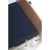 Hospital bed with Sidhil Acclaim Bariatric VE Mattress Extension and light wood headboard, close-up.