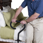 Stander Bed Cane in use helping a person stand from a divan bed with green and white bedding, side view.