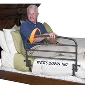 Man on bed holding Stander 30 Inch Safety Bed Rail pivoting down 180° with orange arrow for fall prevention, side view.
