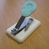 Easi-Grip table-top finger nail clipper with light blue lever and cream base, shown on a wooden surface, top view.