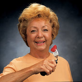 Older woman holding a Good Grips Fork with an adaptive handle, dark background, in use view.