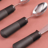 Three dessert spoons with large ribbed black handles and metal ends on a pink background, diagonal top view.