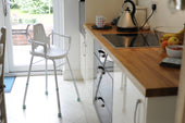 Prima Modular Perching Stool with arms and back by a wooden kitchen counter, side view.