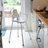 Prima Modular Perching Stool with arms and back by a wooden kitchen counter, side view.
