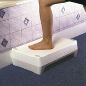 Barefoot person stepping onto a white bath step on tiled bathroom floor with blue carpet, in use view.