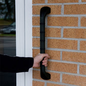 Hand holding a straight outdoor grab bar with anti-slip grip, fixed vertically to a brick wall near a glass door, in use.