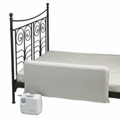 Black metal bed with cream safety rail, Mangar Leglifter and white air pump on floor, side view.
