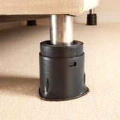 Bed leg with Langham SureGrip in a black furniture raiser lifting the bed on a beige carpet, close-up view.