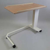 Overbed table with light wood top, white frame, and four wheels on a wheelchair base, side angle view.
