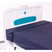 Hospital bed with navy blue foam mattress extension, white headboard, blue label, and side safety bumpers, side view.