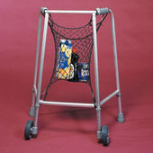 Net bag attached to walking frame holding groceries, with juice and cans inside, red background, front view.
