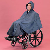 Dark blue wheelchair poncho with knee protection worn by seated person, pink background, front view.