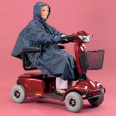 Person in a Homecraft Deluxe Scooter Poncho on a red mobility scooter, pink background, shown in use.