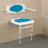 Wall mounted shower seat with blue padded seat and foldable armrests, placed in a tiled bathroom corner, angled view.