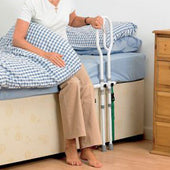Person using Homecraft Bed Grab Rail for support while sitting on bed, one hand on checkered blanket, feet touching floor, in use view.