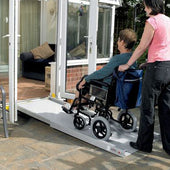 Homecraft Telescopic Broad Ramps in use, assisting a wheelchair user up to glass doors, side view.