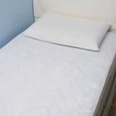 Single bed with Homecraft Caress Waterproof Bedding and white pillow, light blue and white wall in background, side view.