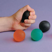 Black gel ball hand exerciser squeezed by hand, orange and green balls nearby on a purple surface, in use close-up.