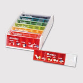 White weekly pill organiser with labelled daily sections, Monday compartment pulled out and containing pills, front angle.