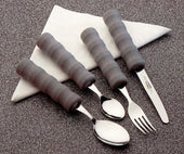 Four lightweight foam-handled cutlery pieces with easy-grip handles on a folded white napkin, speckled surface, top view.