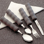 Four lightweight foam-handled cutlery pieces with easy-grip handles on a folded white napkin, speckled surface, top view.