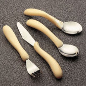 Caring Cutlery set with a fork, knife, and two spoons featuring large curved handles on a grey textured surface, top view.