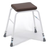 White perching stool with four legs, rubber feet, and brown cushioned seat, front angle.