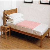 Single wooden bed with white sheets, pink blanket, pillows, and a Kylie Bed Pad with Wings for absorbency, side view.