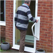 Homecraft Handy Rail in use beside two round plant pots on a brick wall, man opening a glass door, side view.