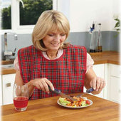 Woman wearing red Homecraft Everyday Bib eating with adaptive utensils at kitchen table, juice on side, in use view.